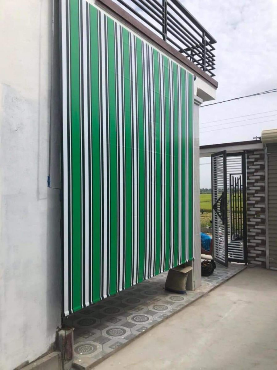 Rèm bạt sọc xanh trắng thả dọc bên ngoài tường nhà cạnh lối đi
