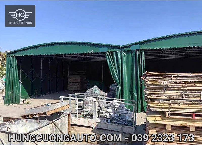 Hai khoang nhà bạt xanh có rèm mở, bên cạnh các chồng gỗ và vật tư
