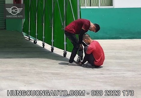 Hai người thao tác tại chân khung gắn bánh xe bên mái bạt xanh